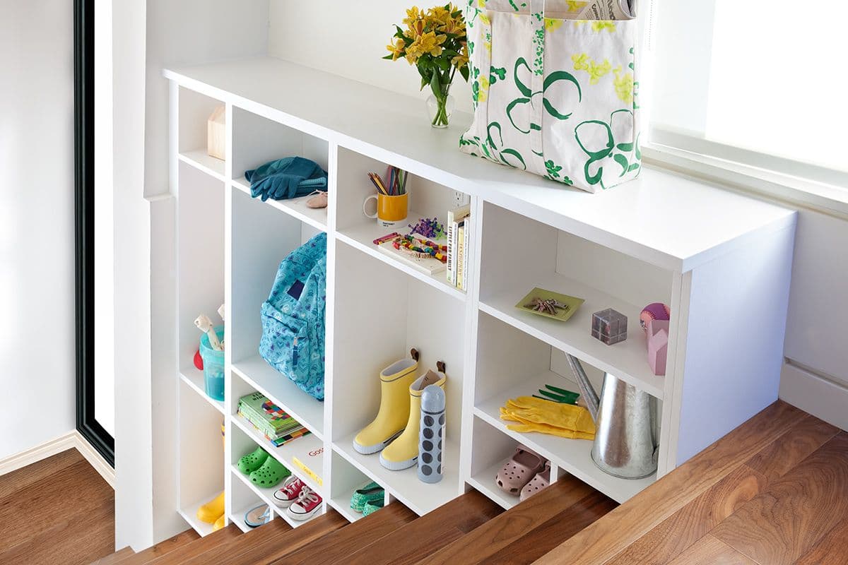 Stairway storage cubbies for kids mudroom designed in white wood finish by California Closets. Activate to enhance image.