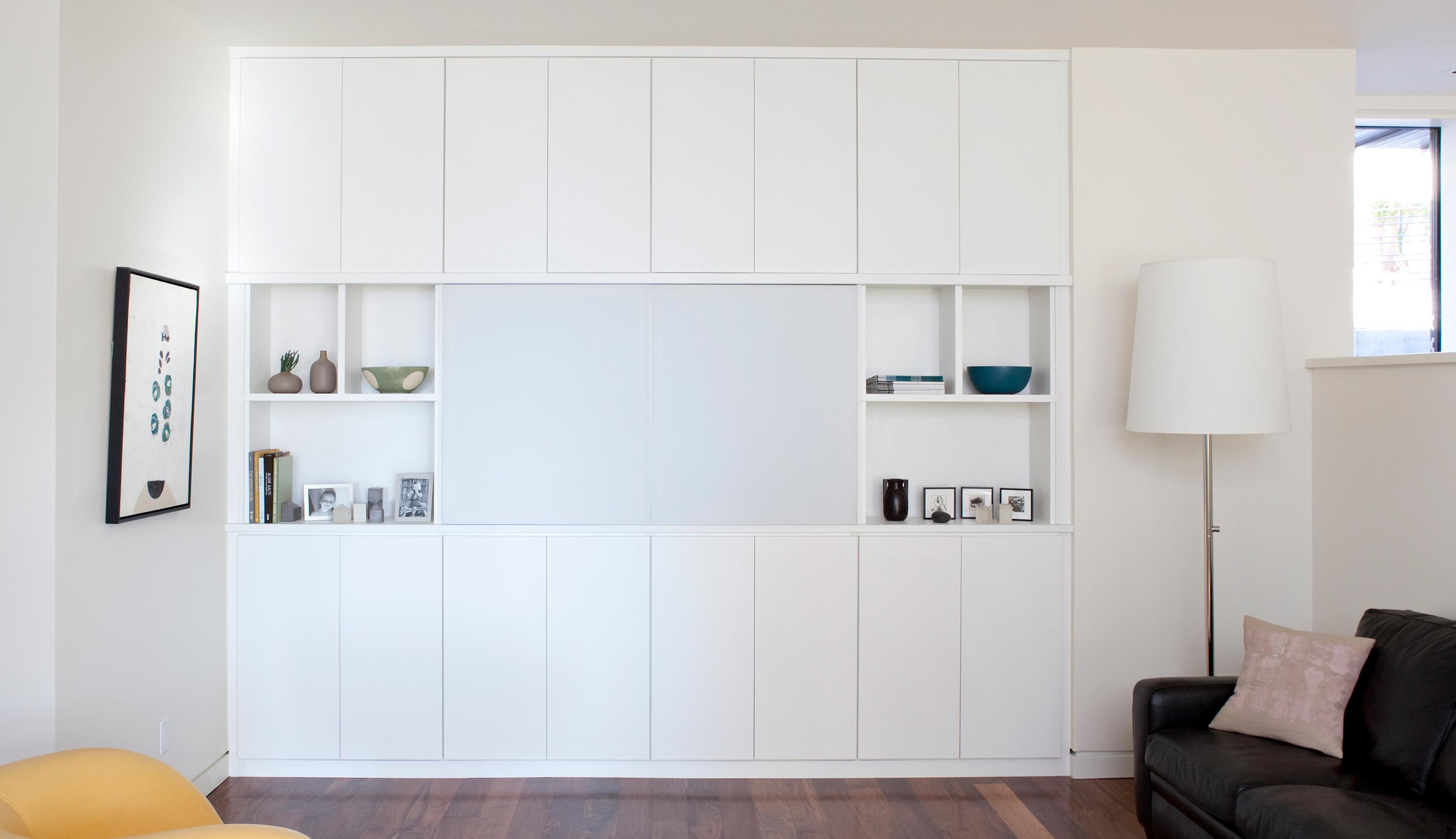 Redesigned entertainment center with white cabinets and custom shelves by California Closets
